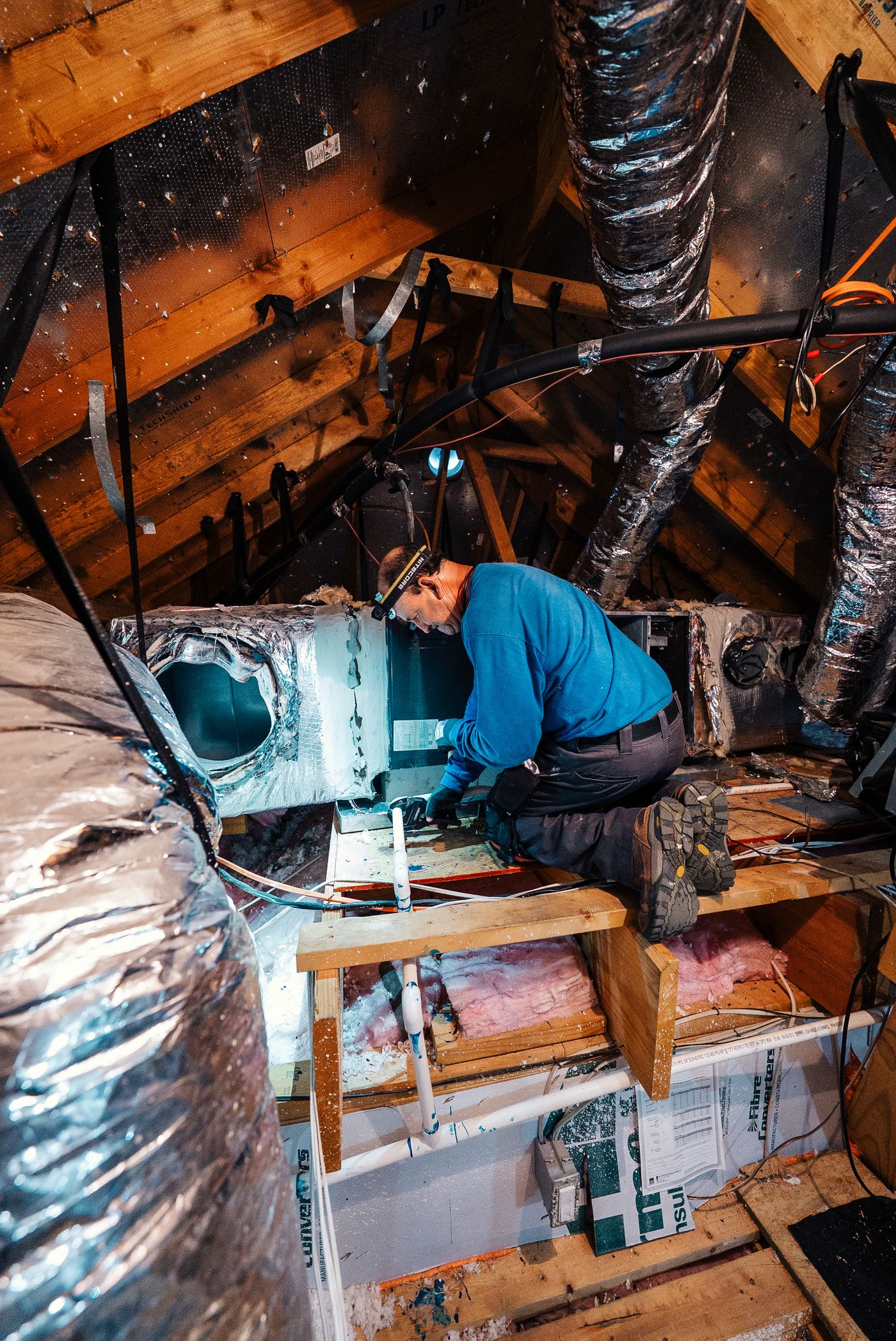 Technician working by headlamp on an attic air handler
