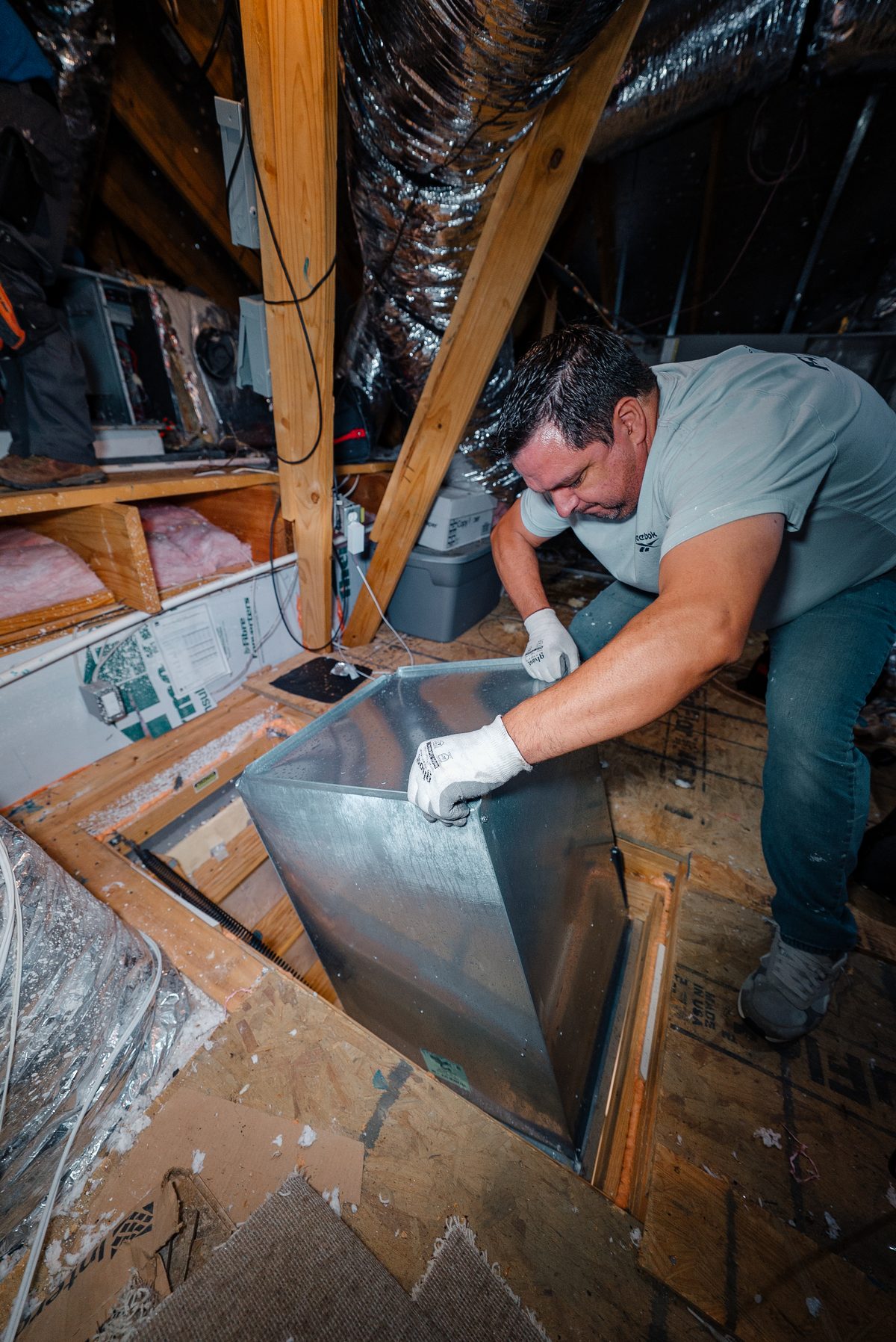 Infinite Home Services technician installing sealed metal ductwork with white gloves